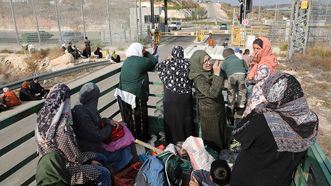 نساء فلسطينيات يقفن في مؤخرة عربة تجرها الجرارات في انتظار عبور نقطة تفتيش عبر الجدار العازل